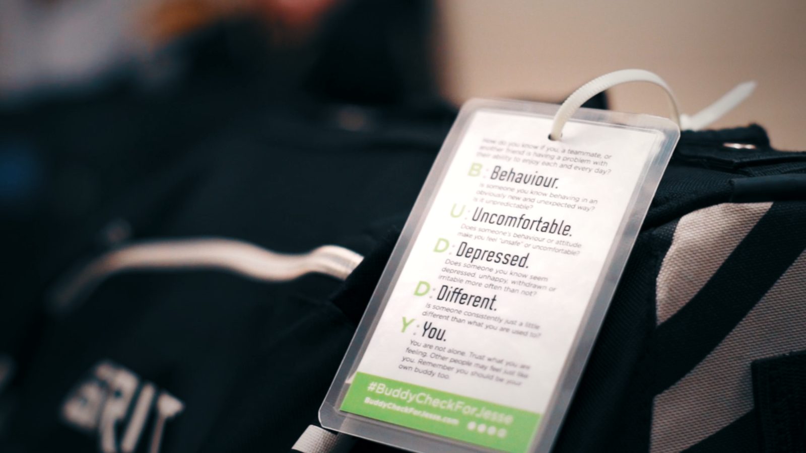 A Buddy Check 'BUDDY' acronym card resting on a hockey bag